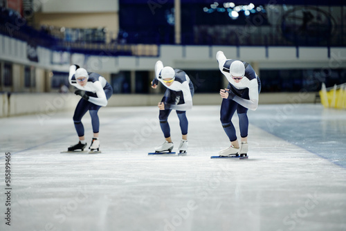Front view of group of young sportsmen in uniform bending forwards while speed skating on ice rink during training or competition