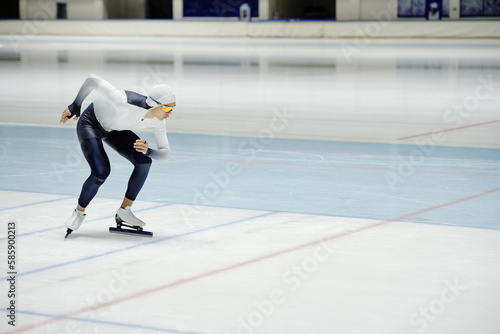 Young speed skater bending forwards while exercising on ice rink and practicing various positions while preparing for competition