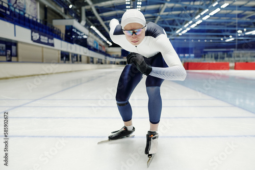 Young sportsman in uniform and eyeglasses standing on skates by start line ready to move forwards during short track speed skating race photo