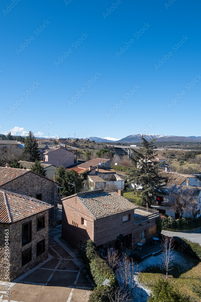 Imagen del pequeño pueblo madrileño de Buitrago de Lozoya con sus casas y la verde montaña al fondo bajo un cielo soleado.