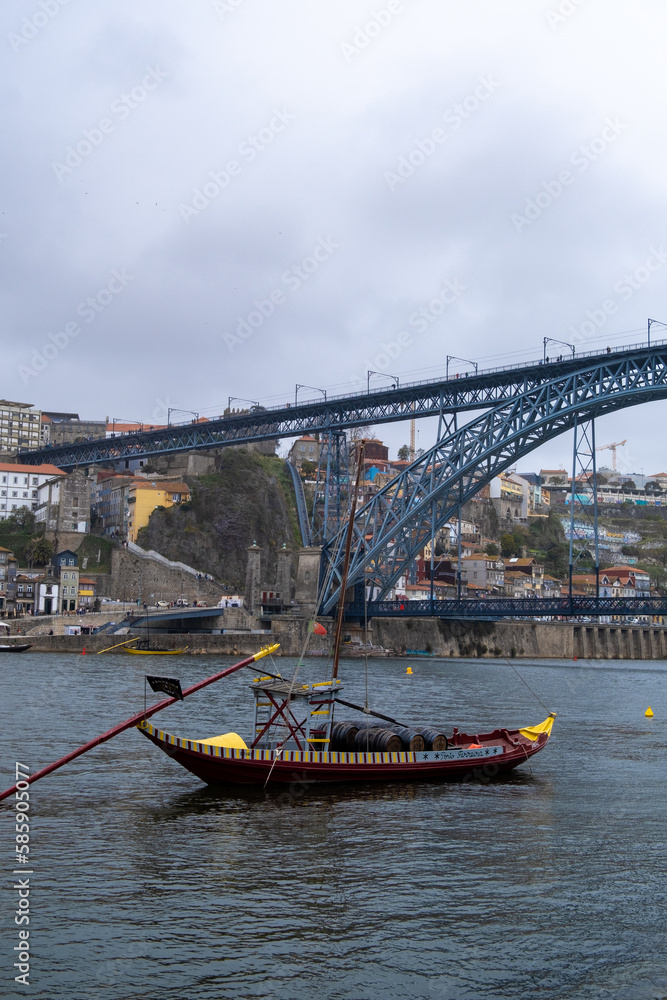Imagen desde abajo del puente de Don Luis I  con un pequeño barco delante en el río de Oporto bajo un cielo nublado en un día de primavera.