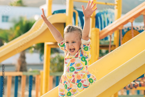 Child playing on outdoor wooden playground. Kids play on school or kindergarten yard. Active kid on colorful slide. Healthy summer activity for children