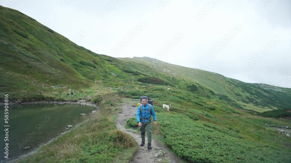 Portrait of a man with a backpack walking next to a lake in the mountains. Boy hiking among beautiful mountains outdoors. The tourist looks around. High quality 4k footage Portrait of a man with a backpack walking next to a lake in the mountains. Boy hiking among beautiful mountains outdoors. The tourist looks around. High quality 4k footage