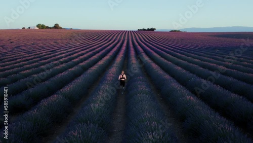 In the pink and purple lavender fields at sunrise, woman runs with a graceful stride. Sport exercise and beauty of nature. Role model or blogger in sports wear. Healthy lifestyle.  photo