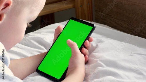 The child is holding a phone with a green screen. Online training. Communication online. phone in hand