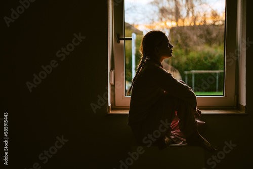 Young bored millennial woman looking at window alone at home. Fatigue or emotionally exhausted concept