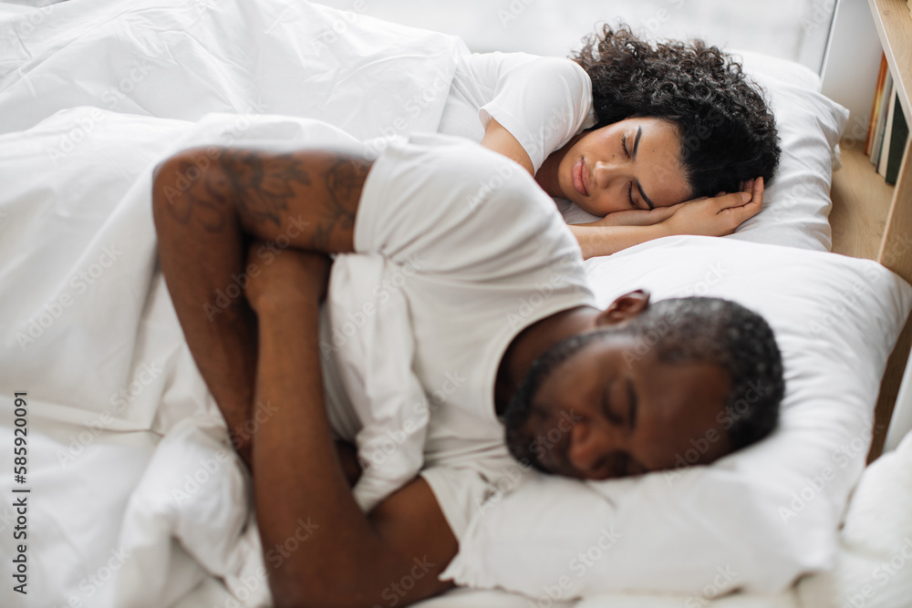 Young multicultural family of two in casual clothing having deep dream before awaking early in morning. Romantic partners sharing relationship closeness by sleeping on same sides under one blanket. Young multicultural family of two in casual clothing having deep dream before awaking early in morning. Romantic partners sharing relationship closeness by sleeping on same sides under one blanket.