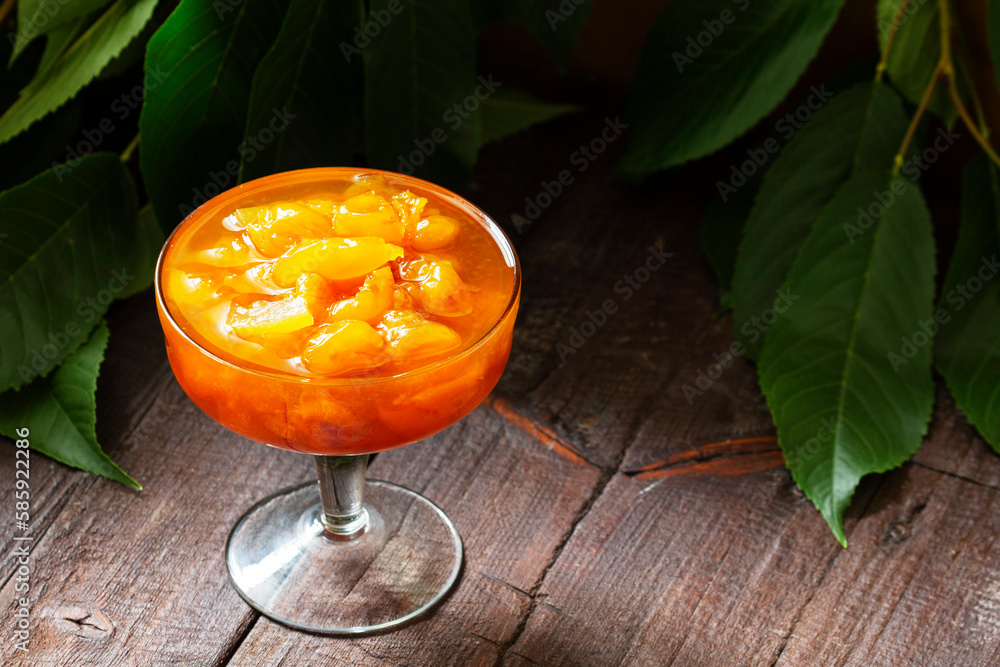 Yellow cherry jam with lemon and vanilla in a glass bowl on a wooden background.