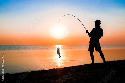 A Happy guy fisherman catching fish by the sea on nature silhouette travel © Kostia