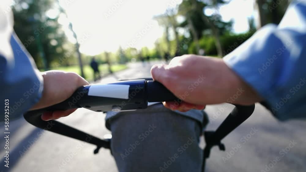 Parent strolling outside at park holding baby carriage handle. POV of mother pushing stroller during sunny day outdoors Parent strolling outside at park holding baby carriage handle. POV of mother pushing stroller during sunny day outdoors