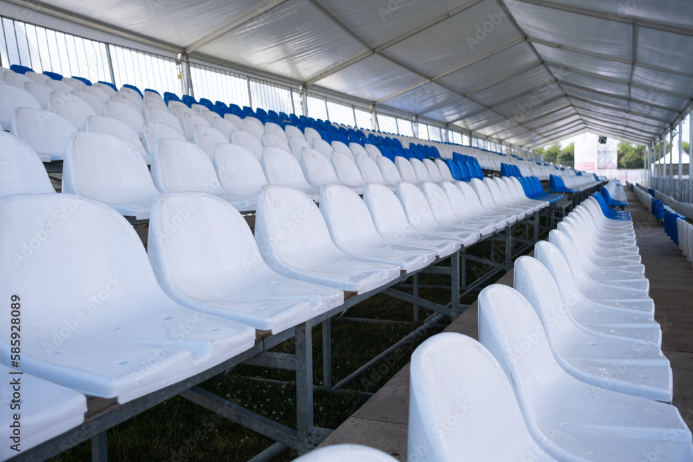 Fototapeta premium Empty white seats of tribune on sport stadium. Many empty plastic seats in rows in an outdoor stadium. Concept of fans, chairs for audience