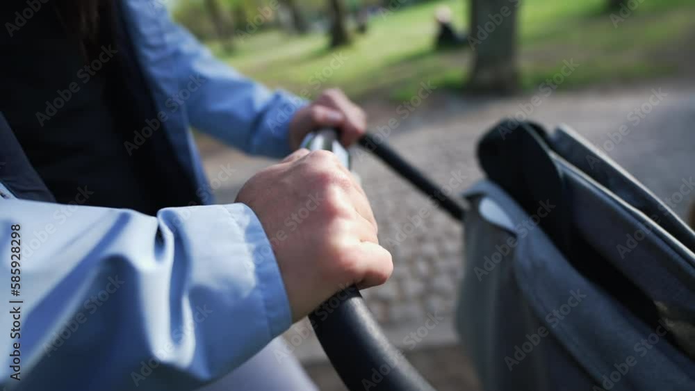 Mother pushing baby carriage closeup hand holding stroller handle. Parent strolling outside at park during sunny day Mother pushing baby carriage closeup hand holding stroller handle. Parent strolling outside at park during sunny day