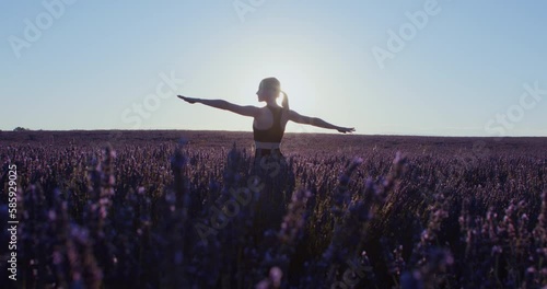 Dreamy girl in sports wear practices meditational yoga asanas in lavender fields at sunrise, inspiring wanderlust. Warrior pose practice. Stretching exercises. Healthy lifestyle blogger or model.  photo