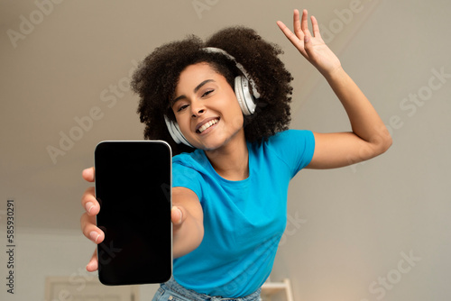 Glad young curly african american lady in wireless headphones listen music, enjoy dance