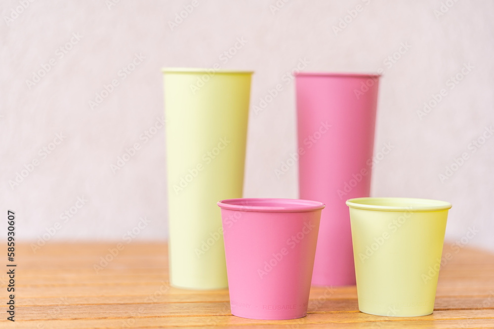 Yellow and pink reusable plastic cups, Bright plastic reusable tableware on a wooden background. Eco cup on the table. The concept of ecology and the absence of garbage Yellow and pink reusable plastic cups, Bright plastic reusable tableware on a wooden background. Eco cup on the table. The concept of ecology and the absence of garbage