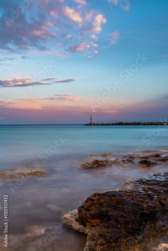 A long exposure sunset on the beach with a lighthouse in the background.