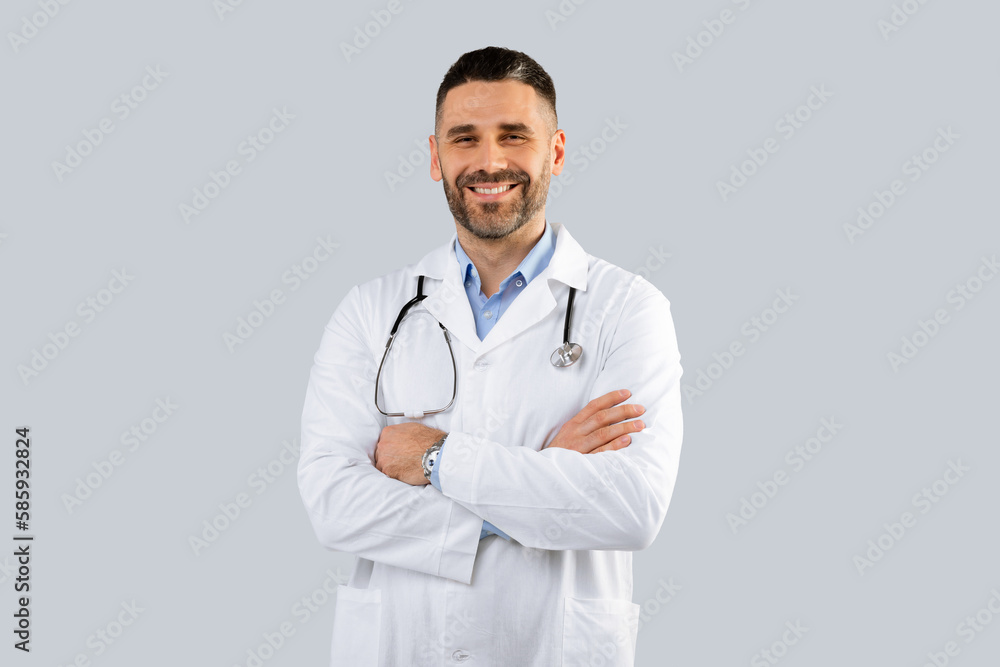 Healthcare, medical staff concept. Portrait of smiling male doctor posing with folded arms, grey background, free space Healthcare, medical staff concept. Portrait of smiling male doctor posing with folded arms, grey background, free space