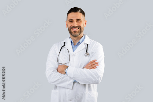Healthcare, medical staff concept. Portrait of smiling male doctor posing with folded arms, grey background, free space