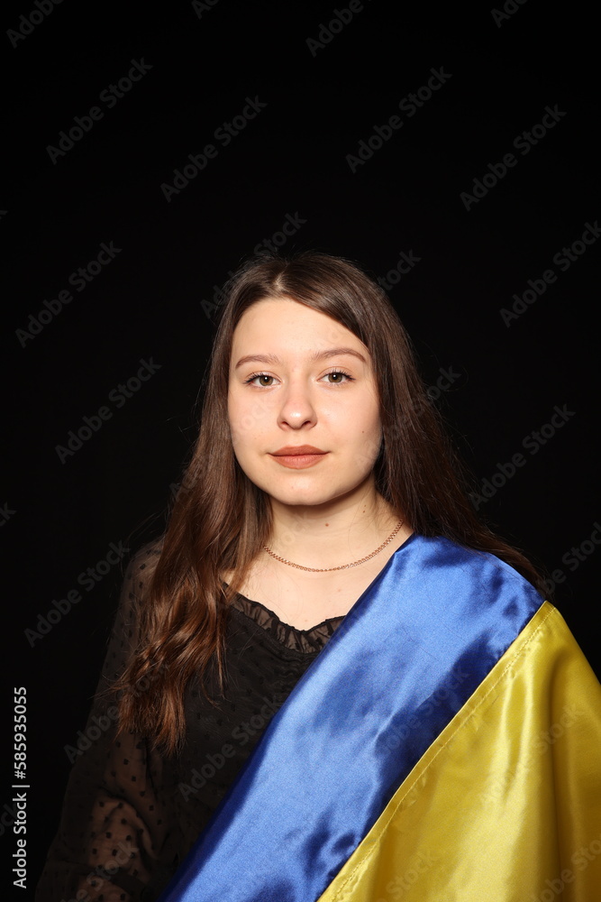 portrait of a beautiful young woman in a black blouse on a black background with the flag of Ukraine. patriot ukrainian girl with yellow and blue flag of ukraine. war in Ukraine