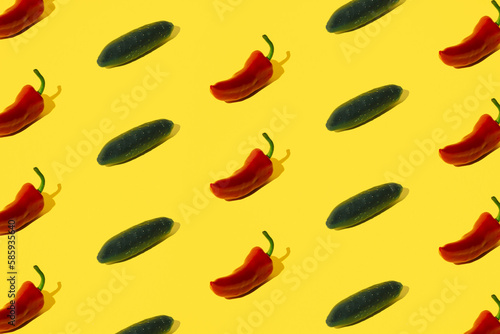 Red pepper and cucumber arranged on a yellow pastel background.