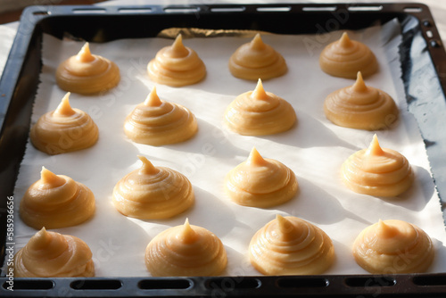 Uncooked French choux pastry dough in a baking tray with sunlight and shadow. It's a preparation step to cook a dessert base of savory choux dough bun  photo