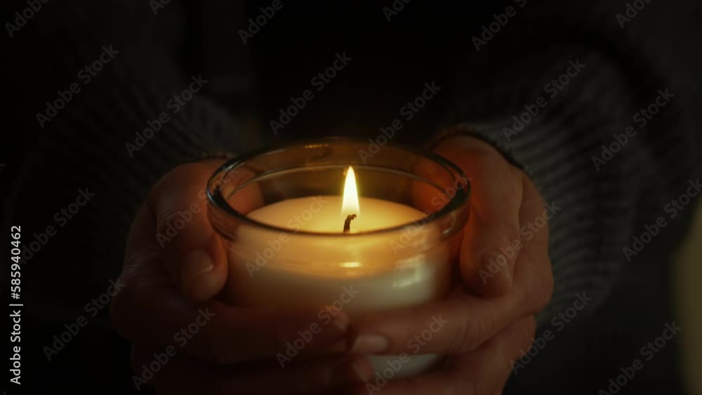 With candle in hands, female meditates and prays, finding peace in flickering flame. Spiritual