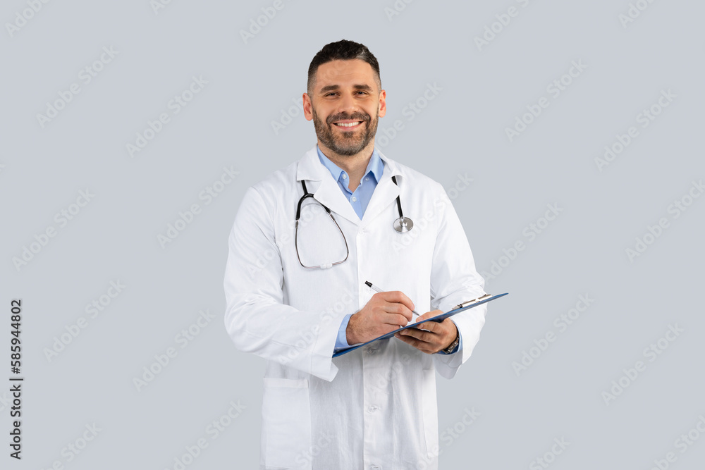 Happy middle aged man doctor in white coat with stethoscope, holding clipboard and smiling at camera, grey background Happy middle aged man doctor in white coat with stethoscope, holding clipboard and smiling at camera, grey background