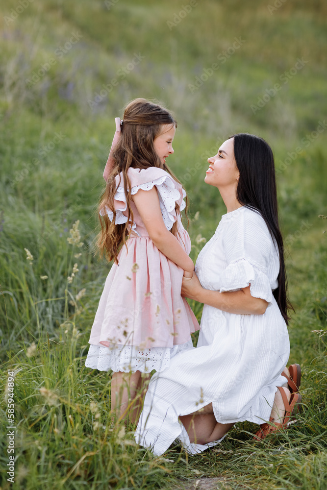 Mothers Day, Women's day. Happy young beautiful mother is hugging her little daughter in the green meadow on summer day. Mom with child are spending time together on nature. World Children day.