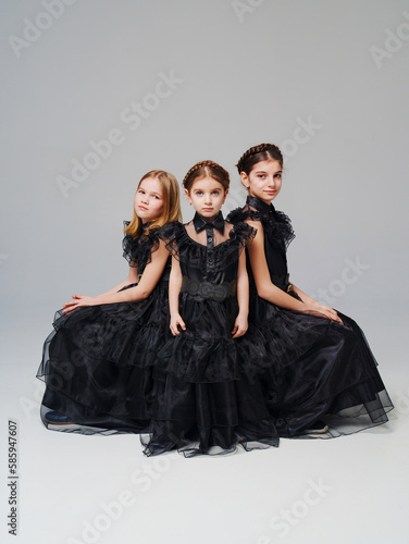 three cute girls in a black long curvy dress on a gray background. 