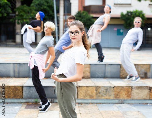 Confident teen girl street dancer posing during performance with group in summer city .