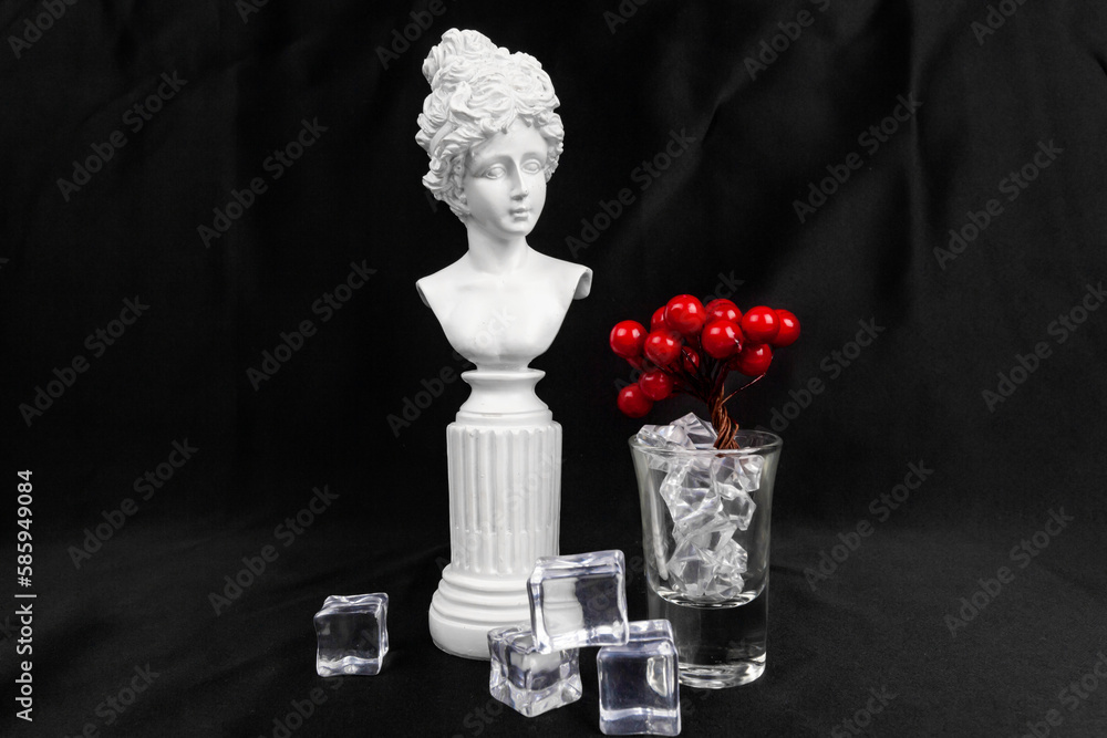 Creative combination of statuette and a glass shot with ice and berries. isolated on black.