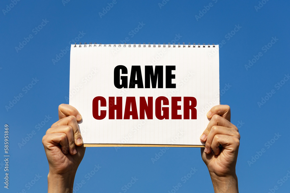 Game changer text on notebook paper held by 2 hands with isolated blue sky background. This message can be used as business concept about game changer. Game changer text on notebook paper held by 2 hands with isolated blue sky background. This message can be used as business concept about game changer.