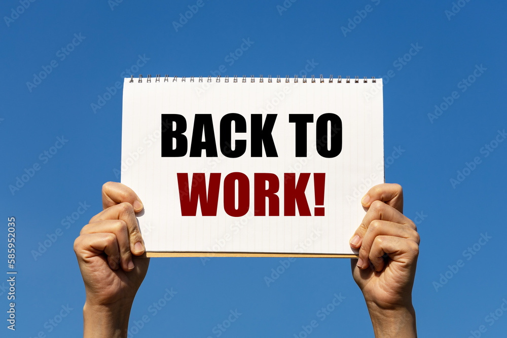 Back to work text on notebook paper held by 2 hands with isolated blue sky background. This message can be used as business concept about going back to work. Back to work text on notebook paper held by 2 hands with isolated blue sky background. This message can be used as business concept about going back to work.