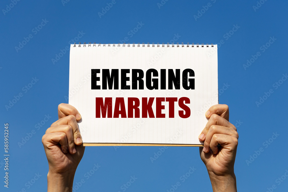 Emerging markets text on notebook paper held by 2 hands with isolated blue sky background. This message can be used as business concept about emerging markets. Emerging markets text on notebook paper held by 2 hands with isolated blue sky background. This message can be used as business concept about emerging markets.