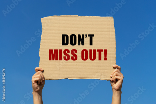 Don't miss out text on box paper held by 2 hands with isolated blue sky background. This message board can be used as business concept about don't miss out.
