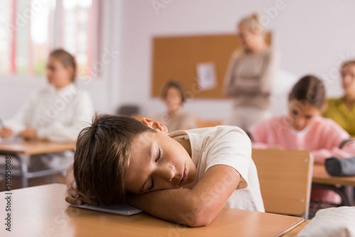 Portrait of tired bored school boy lying and sleeping at desk in classroom during lesson