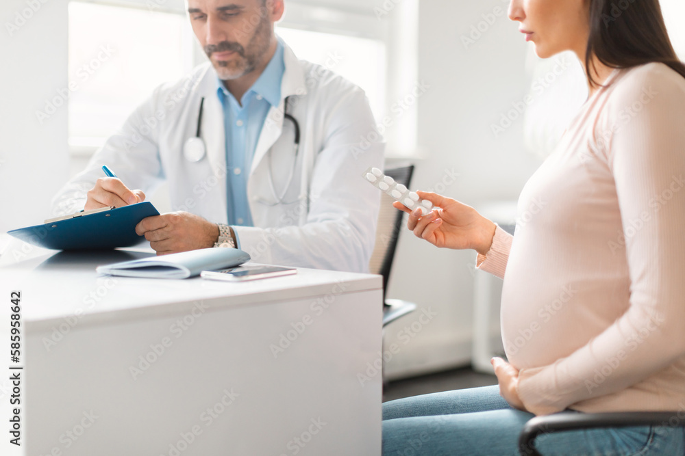 Medication in pregnancy. Male doctor prescribing medicines pills for young pregnant lady, female patient holding tablets Medication in pregnancy. Male doctor prescribing medicines pills for young pregnant lady, female patient holding tablets