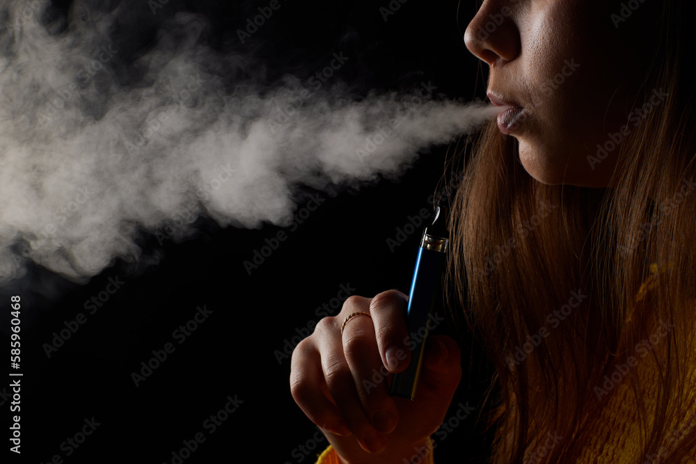 Fototapeta premium young girl smokes a vape close-up on a dark background