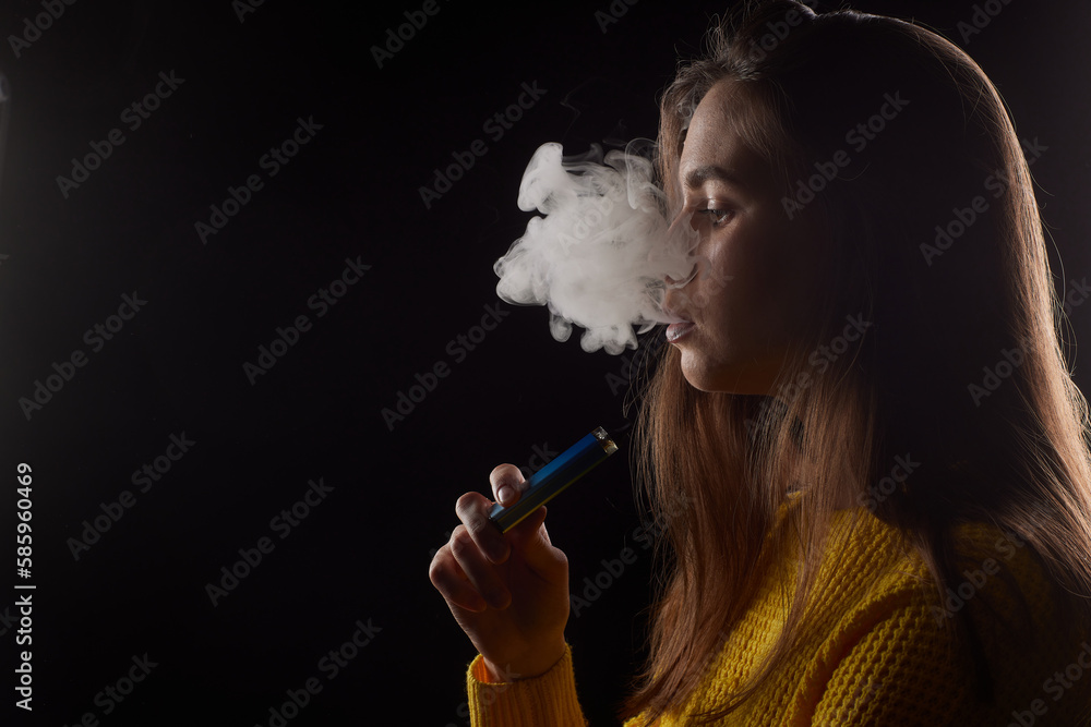Obraz premium young girl smokes a vape close-up on a dark background
