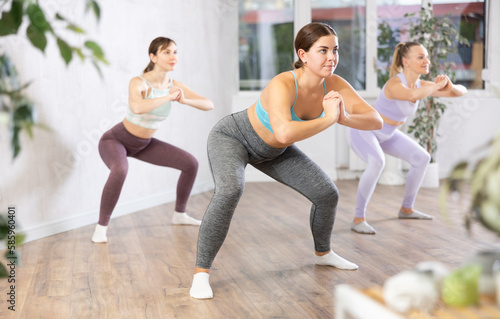 Concentrated young girl doing yoga with group of women in modern studio, performing horse yoga pose to strengthen muscles of legs and buttocks. Bodyweight training concept..