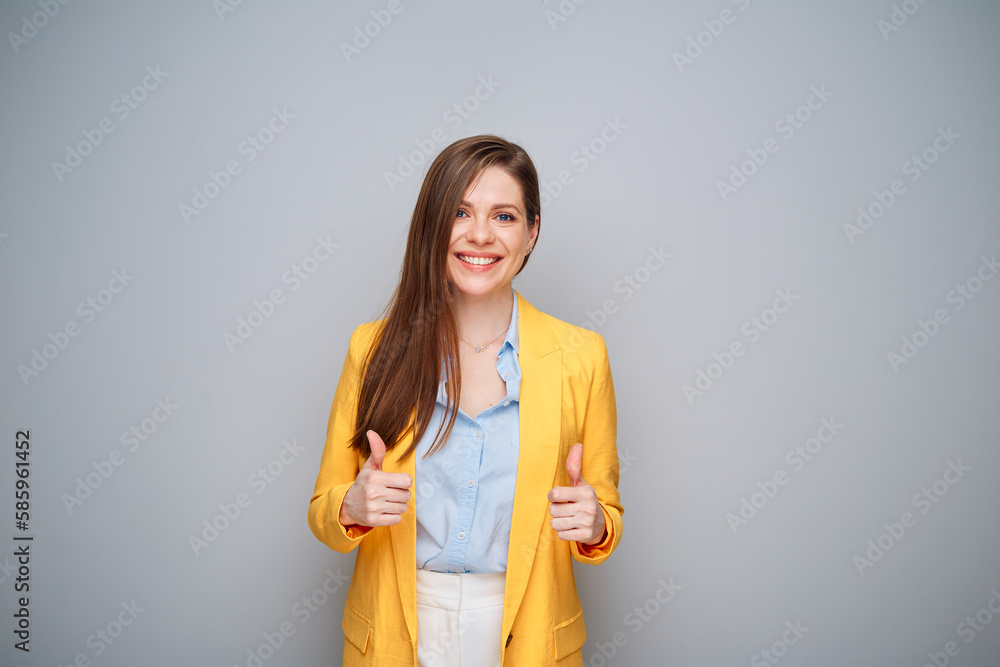 Smiling woman in yellow jacket on gray background showing thumbs up. Smiling woman in yellow jacket on gray background showing thumbs up.
