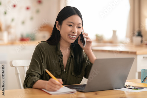 Cheerful asian woman entrepreneur working from home, have phone call