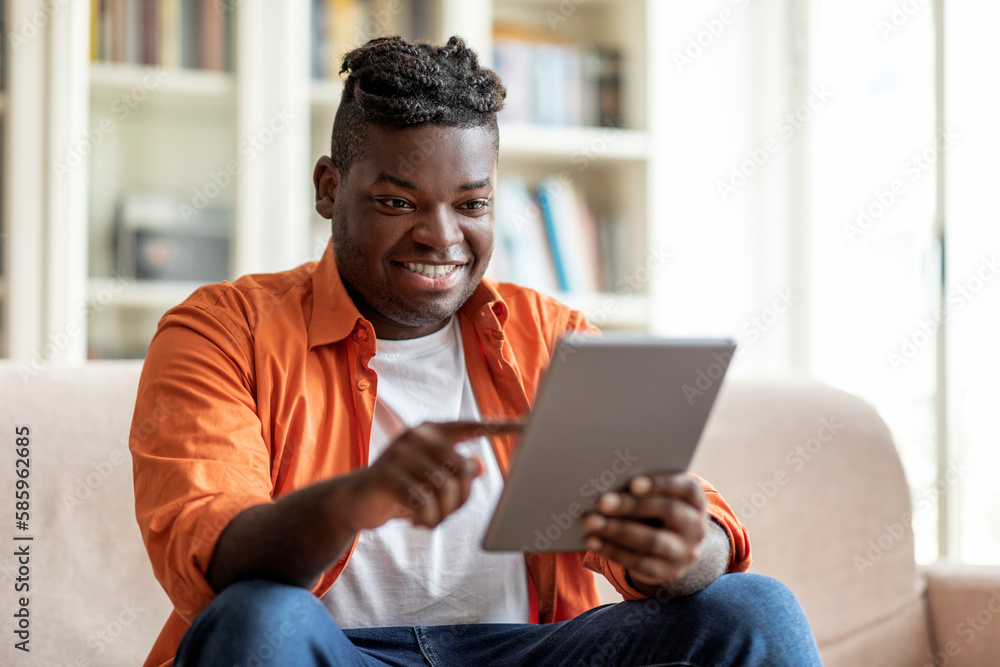 Excited cool overweight black guy using digital tablet at home