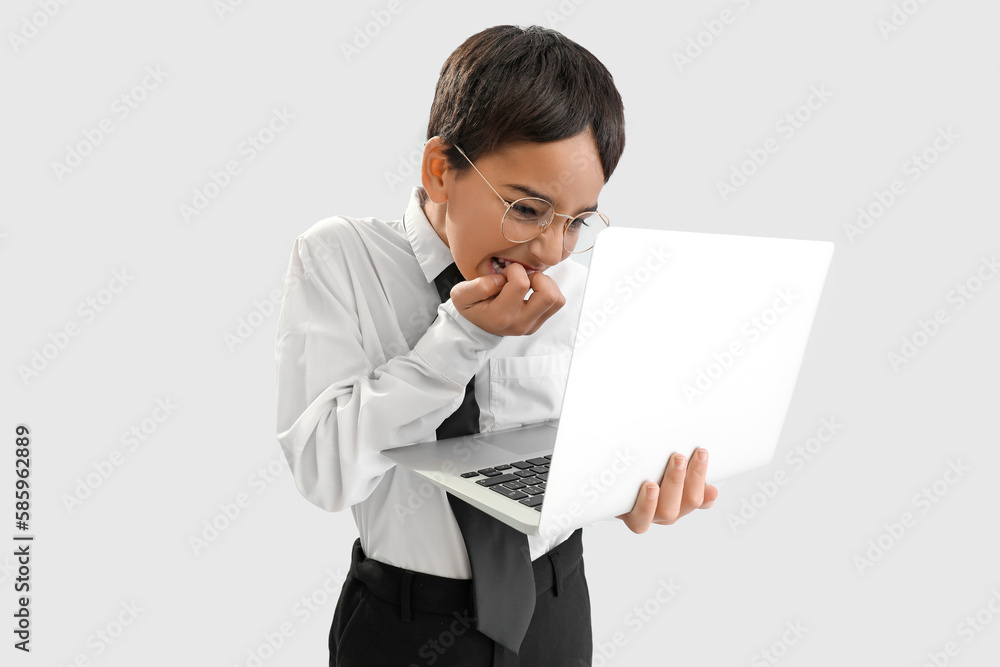 Angry little schoolboy with laptop biting nails on grey background Angry little schoolboy with laptop biting nails on grey background