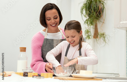 Happy caucasian young mother and teen daughter in aprons make dough for cookies with hands, have fun photo