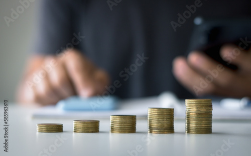 Businessman saving money concept financial. Close-up of coins stacks with blurred hand using smartphone and calculator to calculate in the background. concept of saving money for finance accounting.