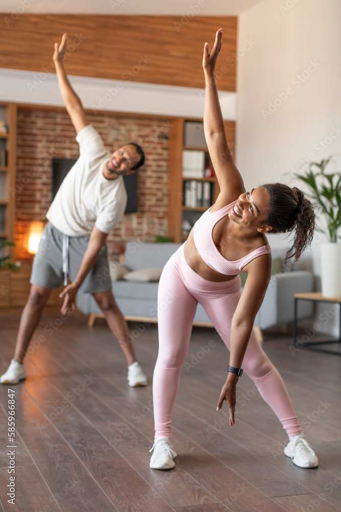 Fototapeta premium Glad happy young black female and male athletes in sports wear do hand exercises on workout together