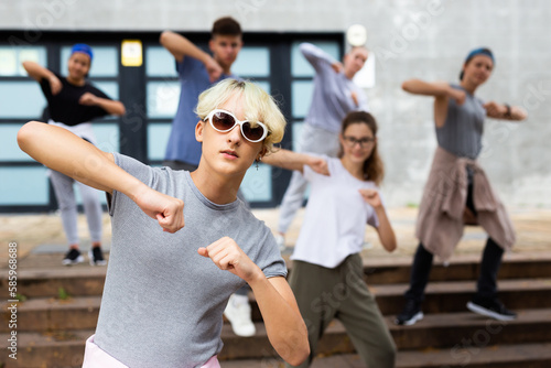 Portrait of modern teenager performing street dance with group of friends outside in summer.