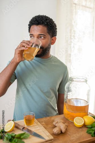 Young black man drinking homemade kombucha drink, flavoured with lemon and mint, healthy drink, organic probiotic beverage