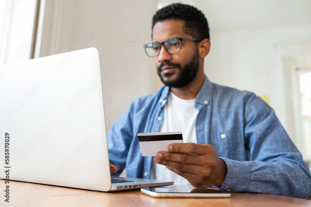 Young handsome cheerful black man working from home online remotely using his laptop. Looking at laptop screen, smiling. Young handsome cheerful black man working from home online remotely using his laptop. Looking at laptop screen, smiling.